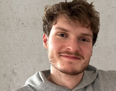 Julian, ein junger Mann mti Dreitagebart, lächelt in die Kamera